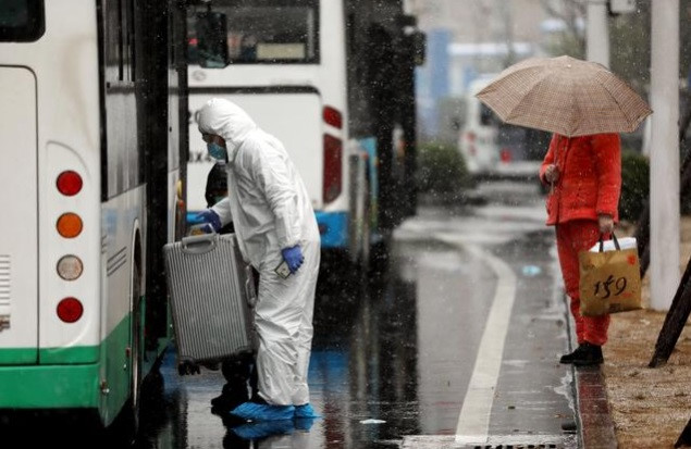Nhân viên mặc đồ bảo hộ nhấc chiếc vali từ xe buýt để bệnh nhân nhiễm virus Corona mới đến một bệnh viện ở Vũ Hán ngày 15.2 /// Reuters