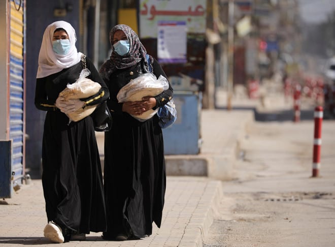 Hai phụ nữ cầm bánh mì trên đi dọc trên con đường vắng vẻ vì lệnh hạn chế đi lại phòng Covid-19 thành phố Qamishli, Syria ngày 23.3 /// Reuters